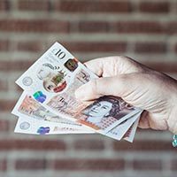 Close up of hand of woman holding pounds sterlings against brick wall background